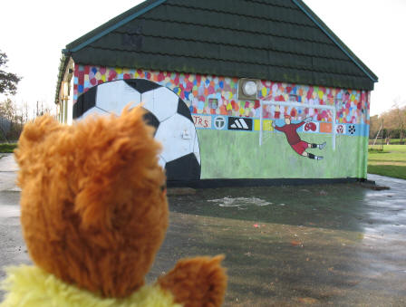 Yellow Teddy admiring football mural on sports hut in Poverest Recreation Ground